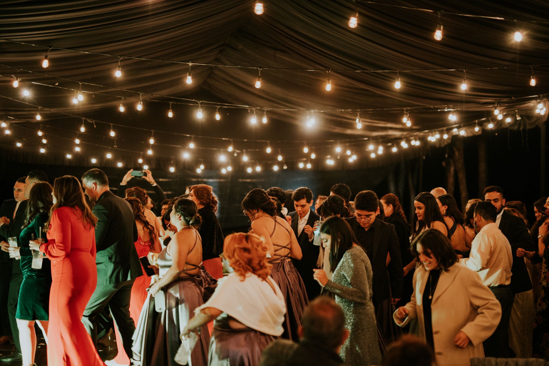Una celebración bajo un techo de guirnaldas de luces cálidas, con invitados compartiendo la pista. Fotografía de inspiración.